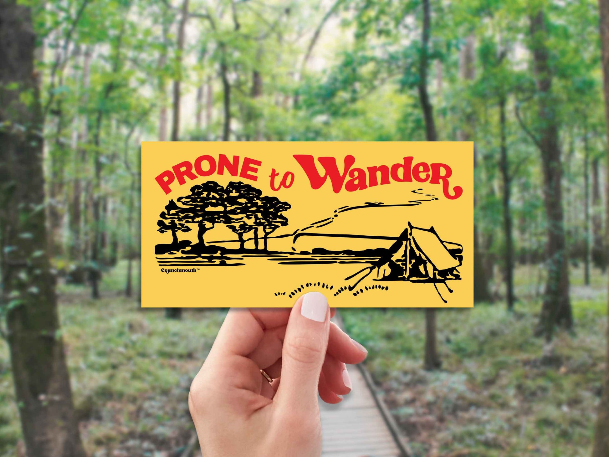 prone to wander camping bumper sticker, hand display, forest background