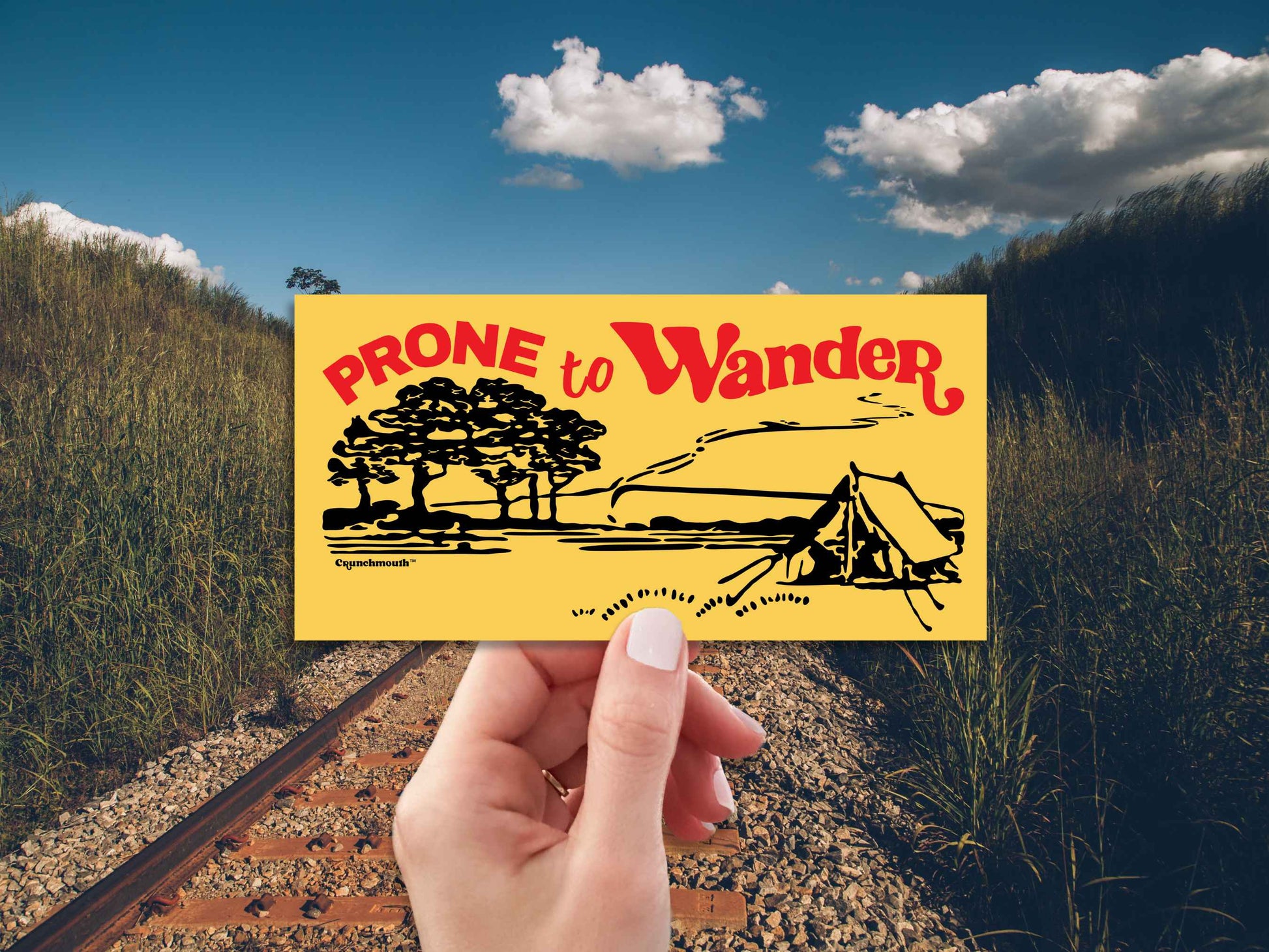 prone to wander camping bumper sticker, hand display, railroad tracks background