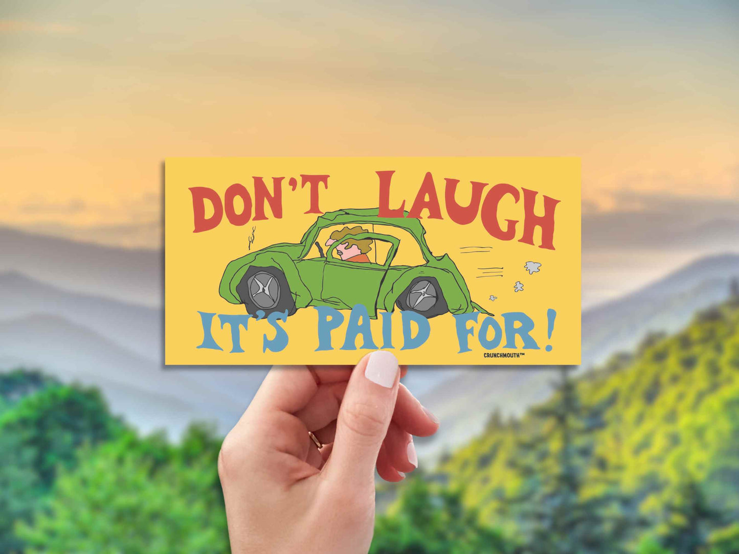 don't laugh it's paid for, funny bumper stickers, hand display, blurred landscape background