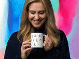 angry goose coffee mug, 11oz, held by woman, handle on right, colorful paint background