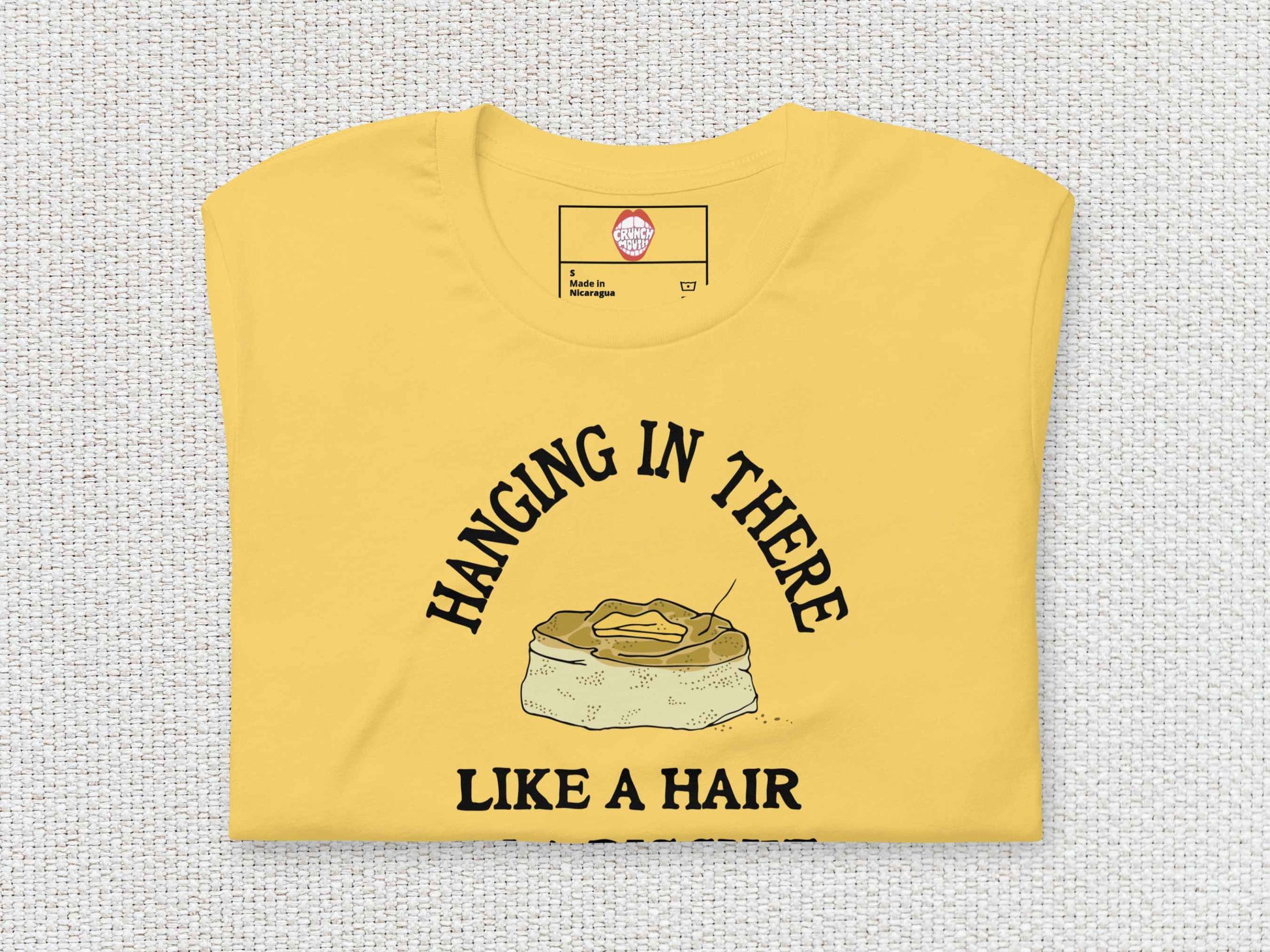 hanging in there like a hair in a biscuit shirt, funny t-shirts, folded, front, white textured background