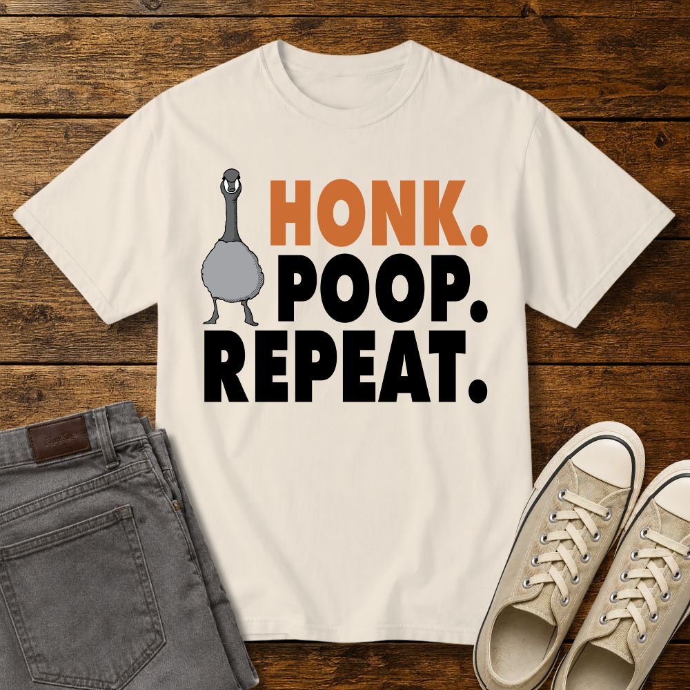 ivory graphic T-shirt mockup featuring a goose illustration and the phrase “Honk. Poop. Repeat.” in bold orange and black lettering, styled with gray jeans and beige sneakers on a rustic wood background.