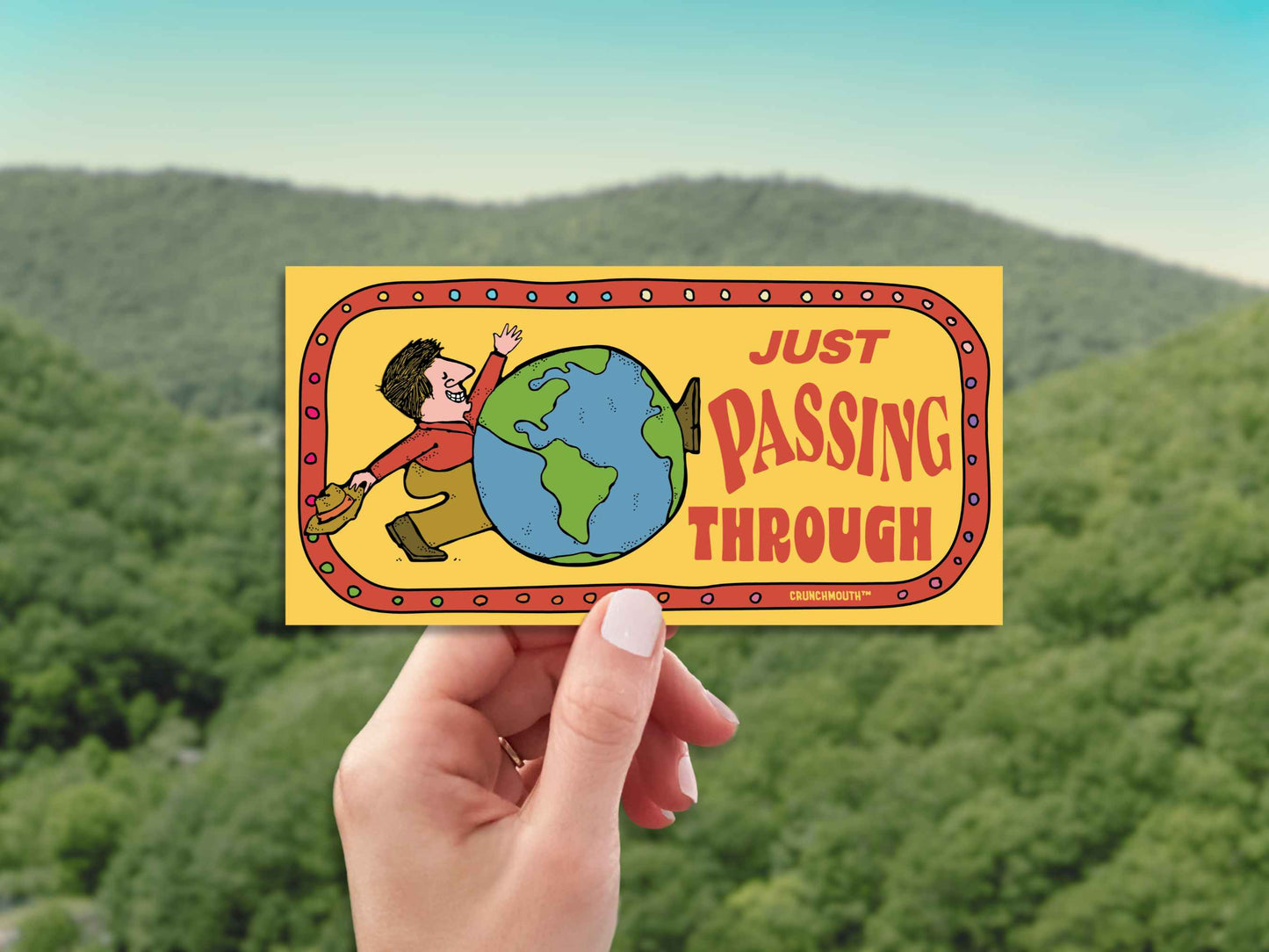 just passing through bumper sticker, hand display, green mountain landscape background