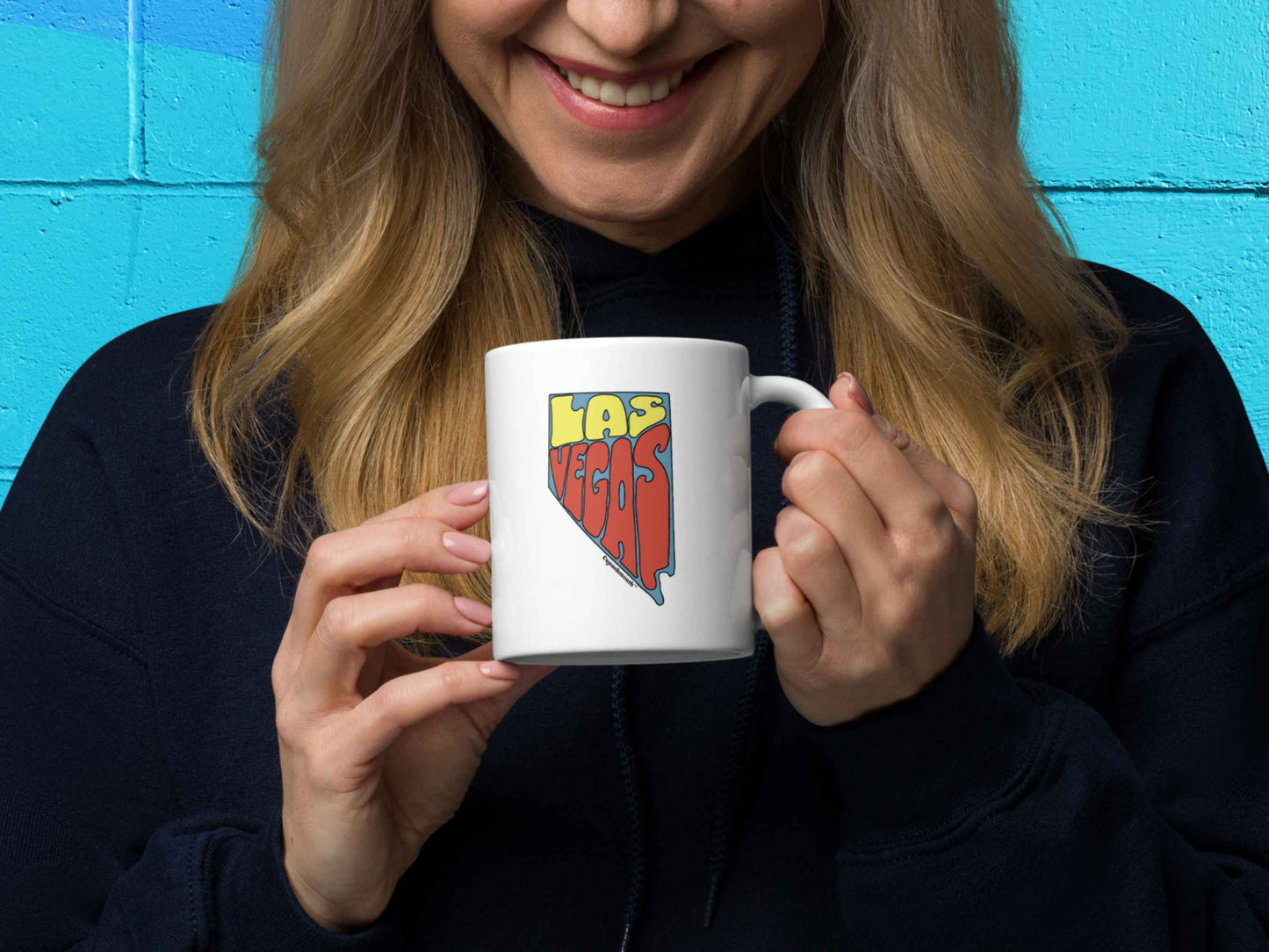las vegas coffee mug, las vegas gifts, 11 oz, handle on right, held by female model, colorful cinder block wall background