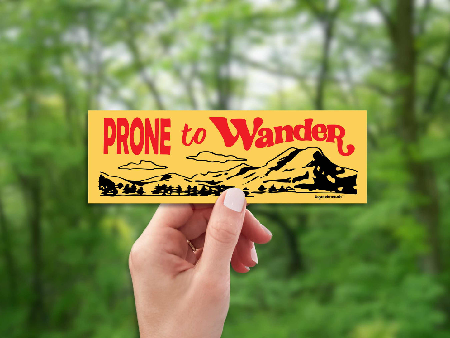 prone to wander bumper sticker, yellow, hand display, blurred forest landscape background