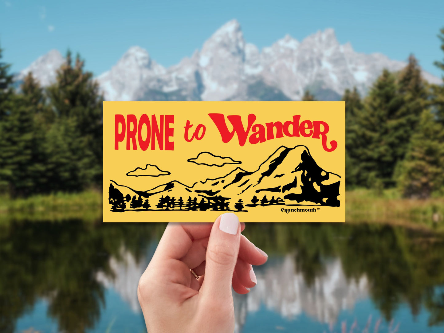 prone to wander bumper sticker, hand display, mountain lake background