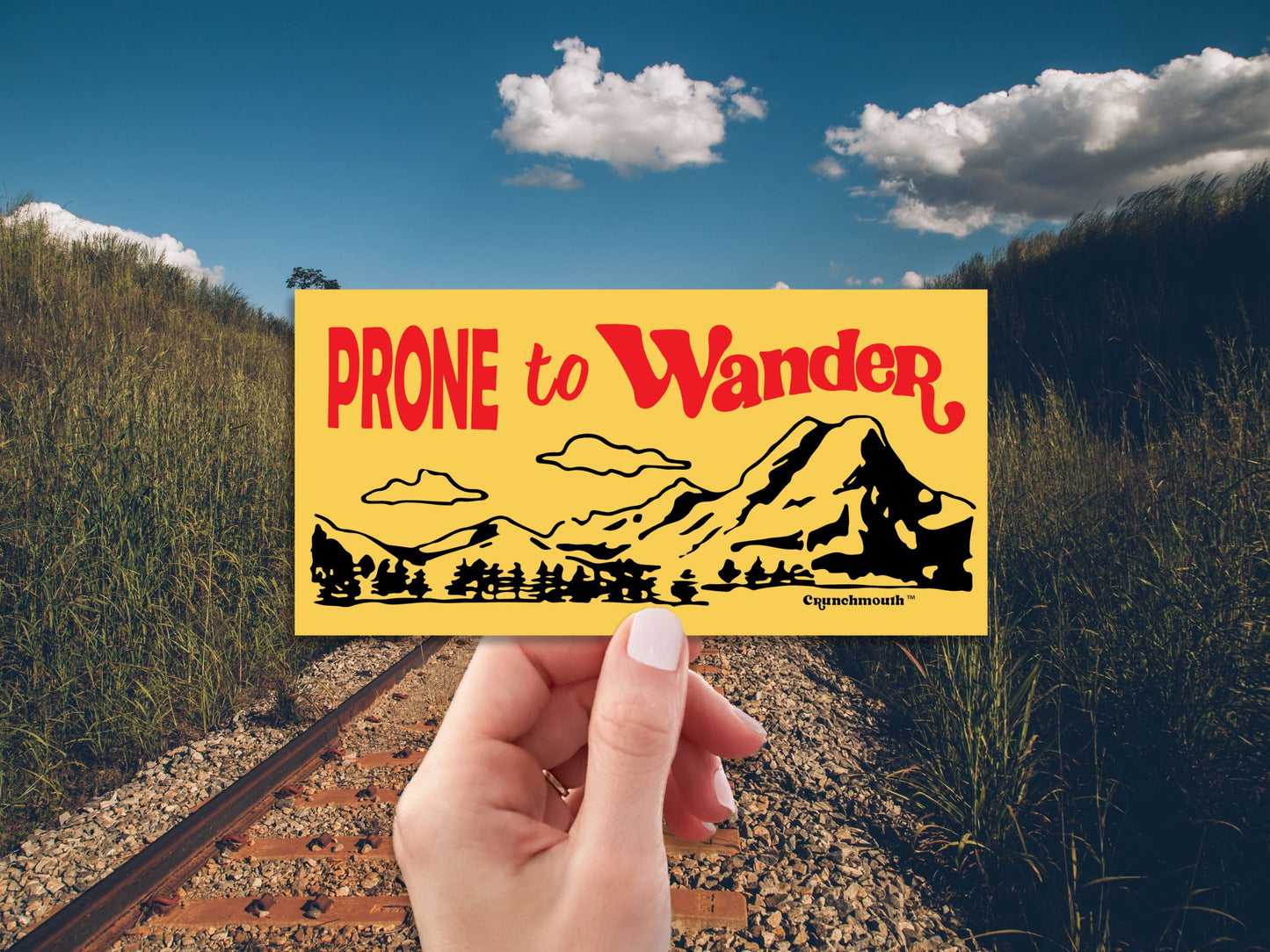 prone to wander bumper sticker, hand display, railroad tracks background