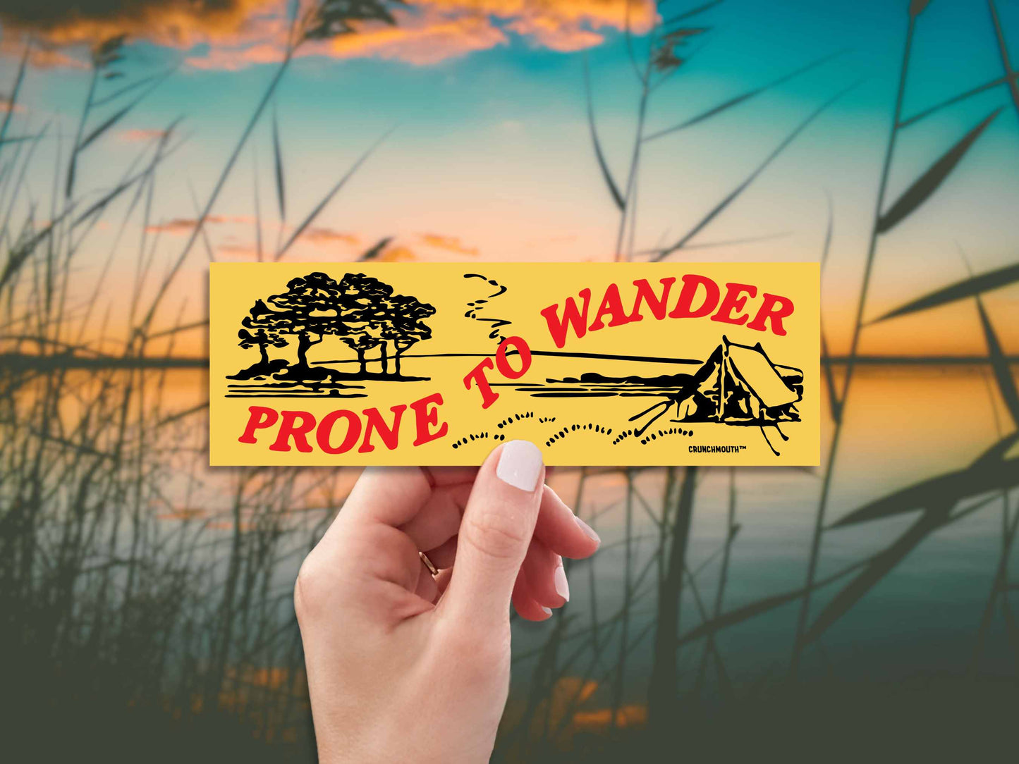 prone to wander camping bumper sticker, hand display, marsh background