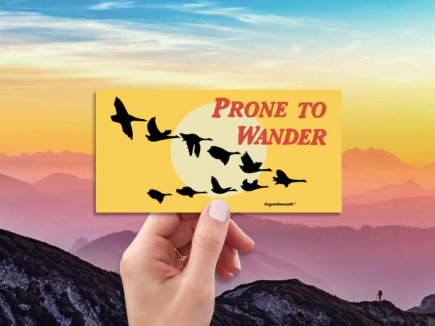 prone to wander bumper sticker, wild geese in the west, hand display, mountain skyline background