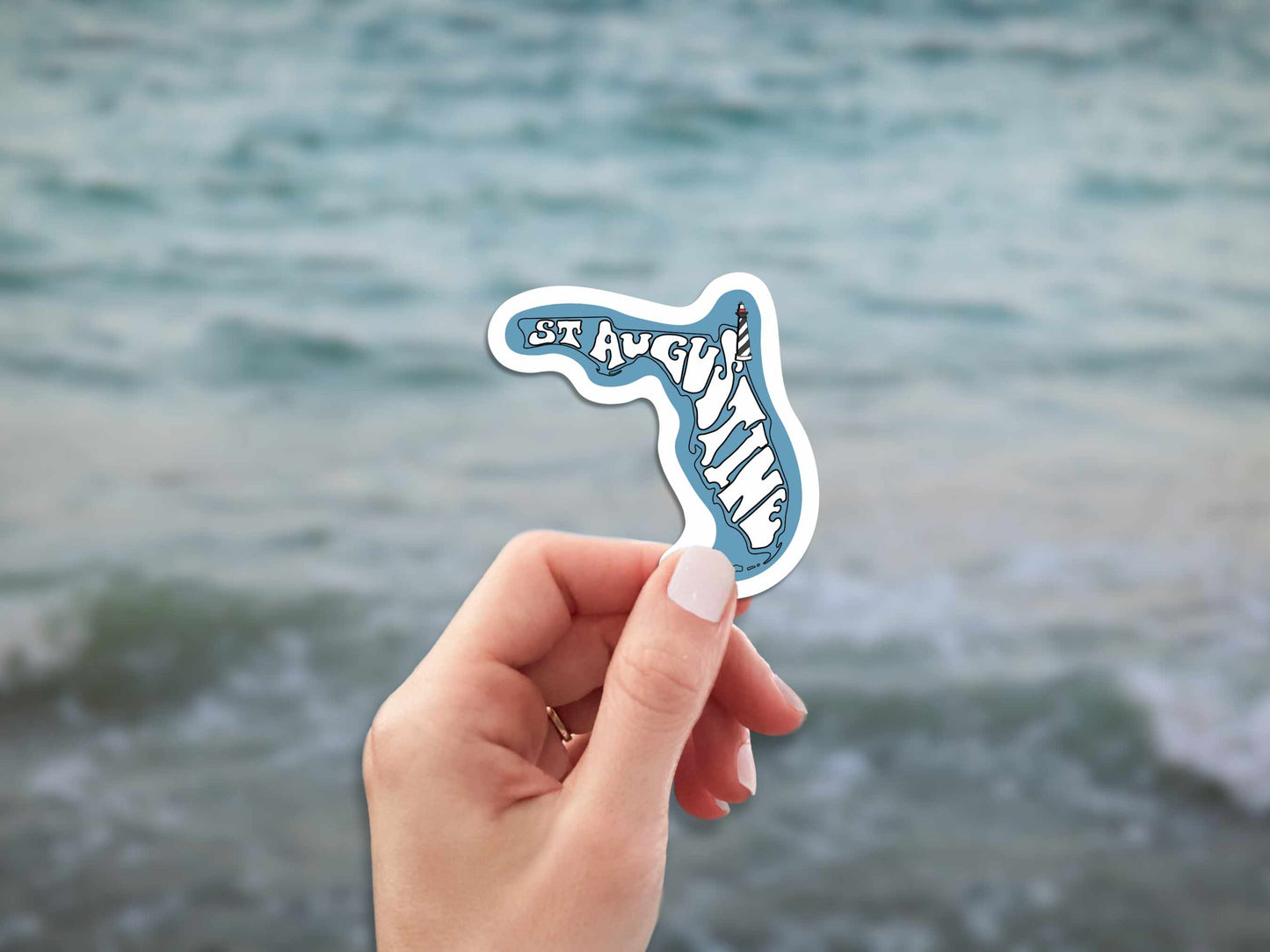 st augustine travel luggage sticker, hand display, blurred ocean water background