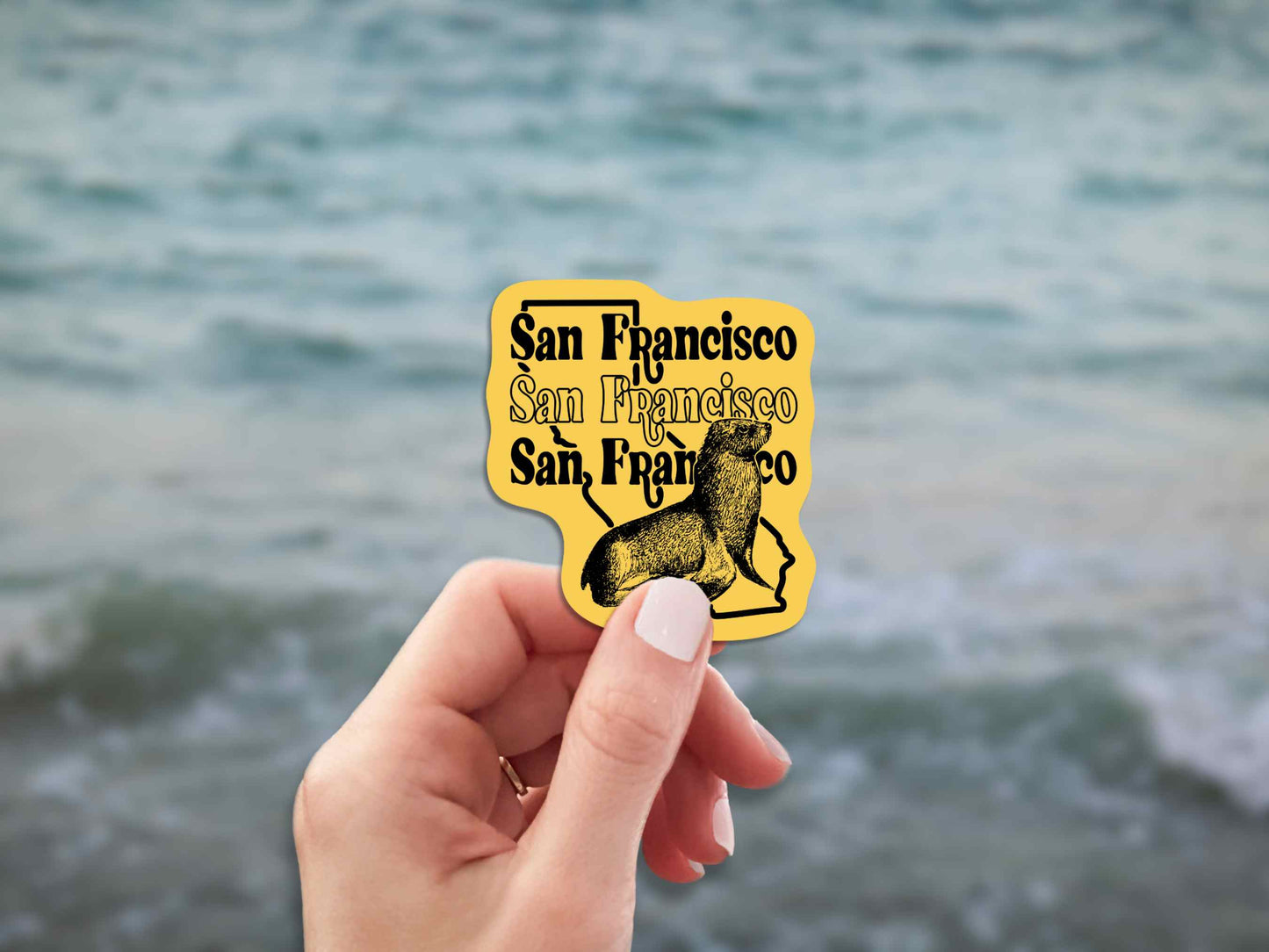 san francisco travel luggage sticker, hand display, blurred ocean water background