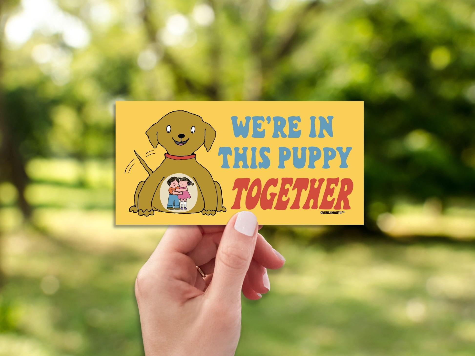 we're in this puppy together bumper sticker, hand display, blurred landscape background