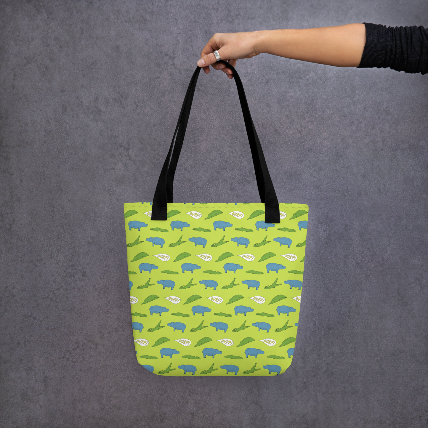 alligator eating hippo pattern tote bag, held in hand against dark background