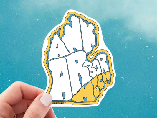 ann arbor sticker, souvenir stickers, held in hand, blue sky background