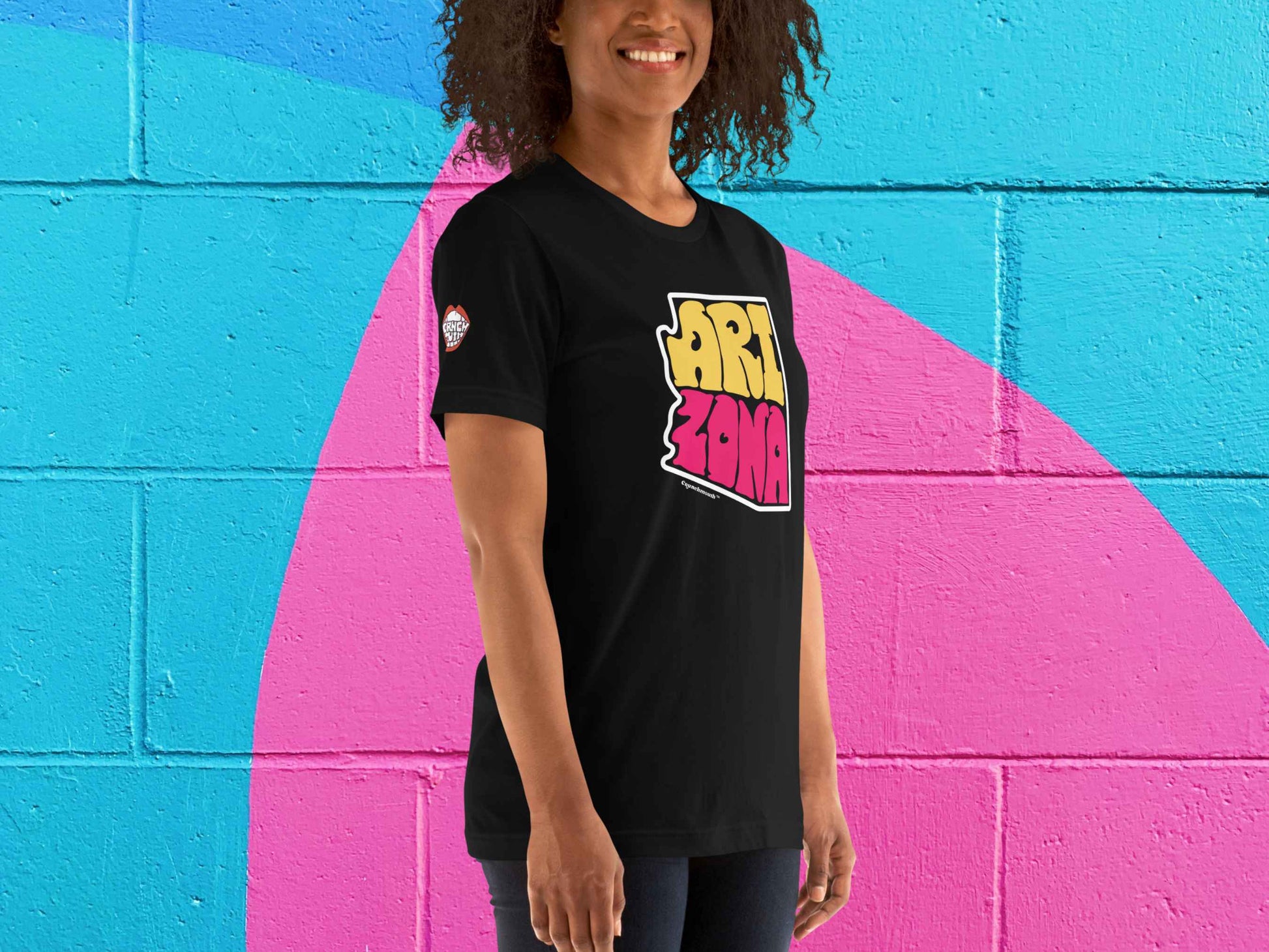 arizona shirt, souvenir t shirts, front right, female model, vibrant color cinder block wall backgroundbackground