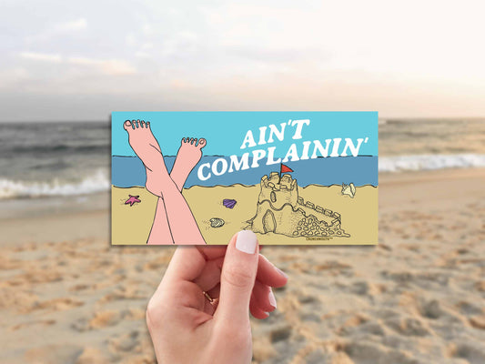 beach vibes bumper sticker, ain't complainin', hand display, beach background