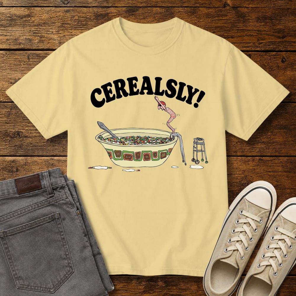 butter yellow graphic T-shirt mockup featuring the phrase “Cerealsly!” above a humorous illustration of an elderly person diving into a giant bowl of cereal, styled with gray jeans and beige sneakers on a rustic wood background.