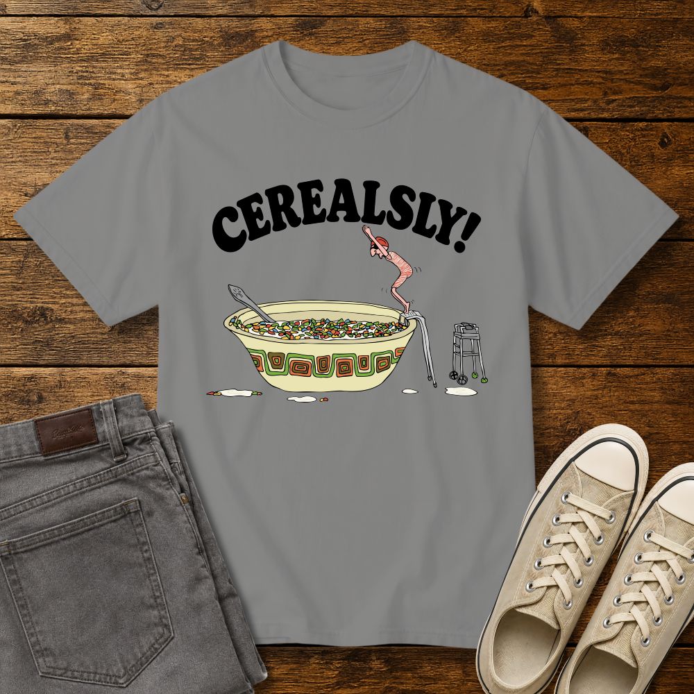 granite grey graphic T-shirt mockup featuring the phrase “Cerealsly!” above a humorous illustration of an elderly person diving into a giant bowl of cereal, styled with gray jeans and beige sneakers on a rustic wood background.