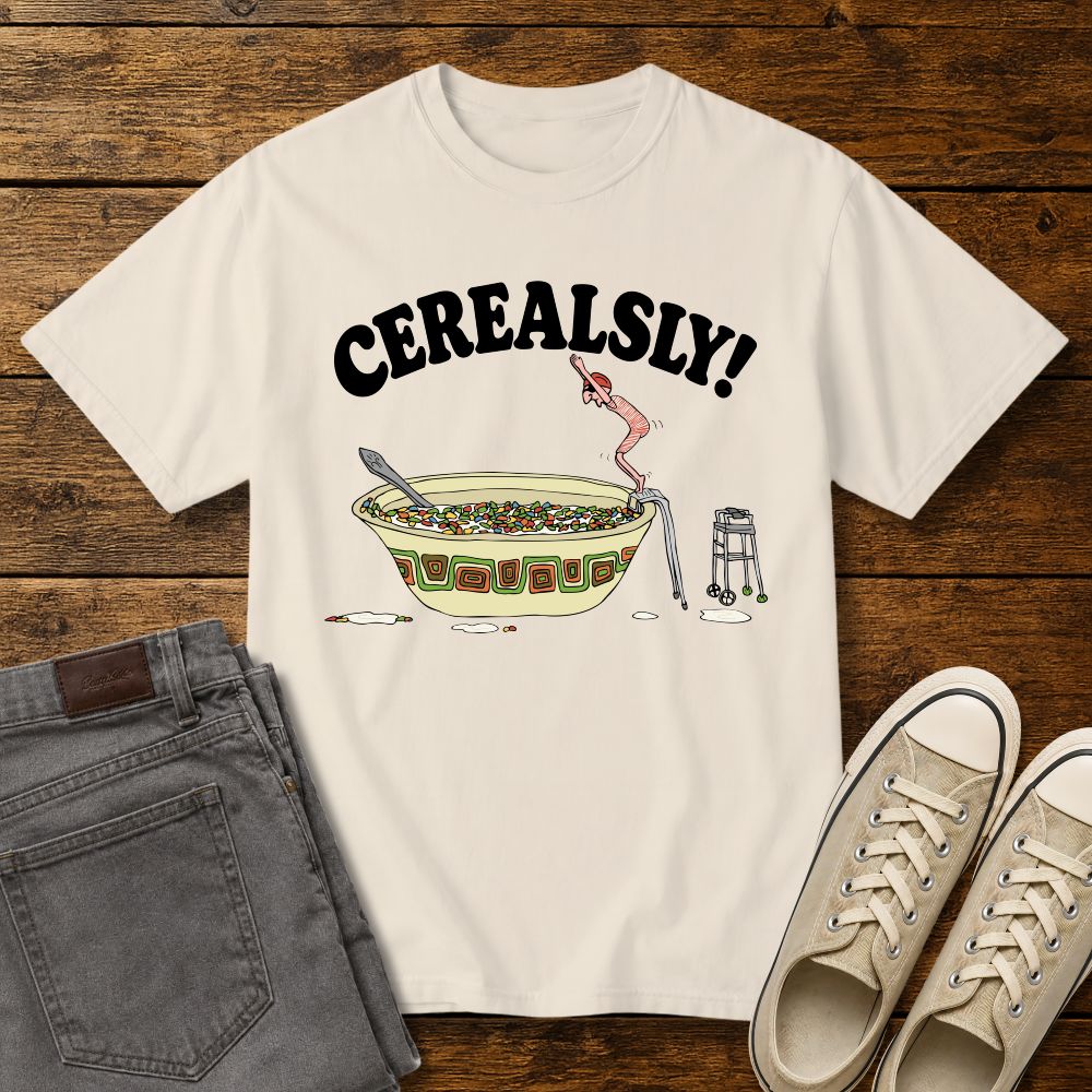 ivory graphic T-shirt mockup featuring the phrase “Cerealsly!” above a humorous illustration of an elderly person diving into a giant bowl of cereal, styled with gray jeans and beige sneakers on a rustic wood background.