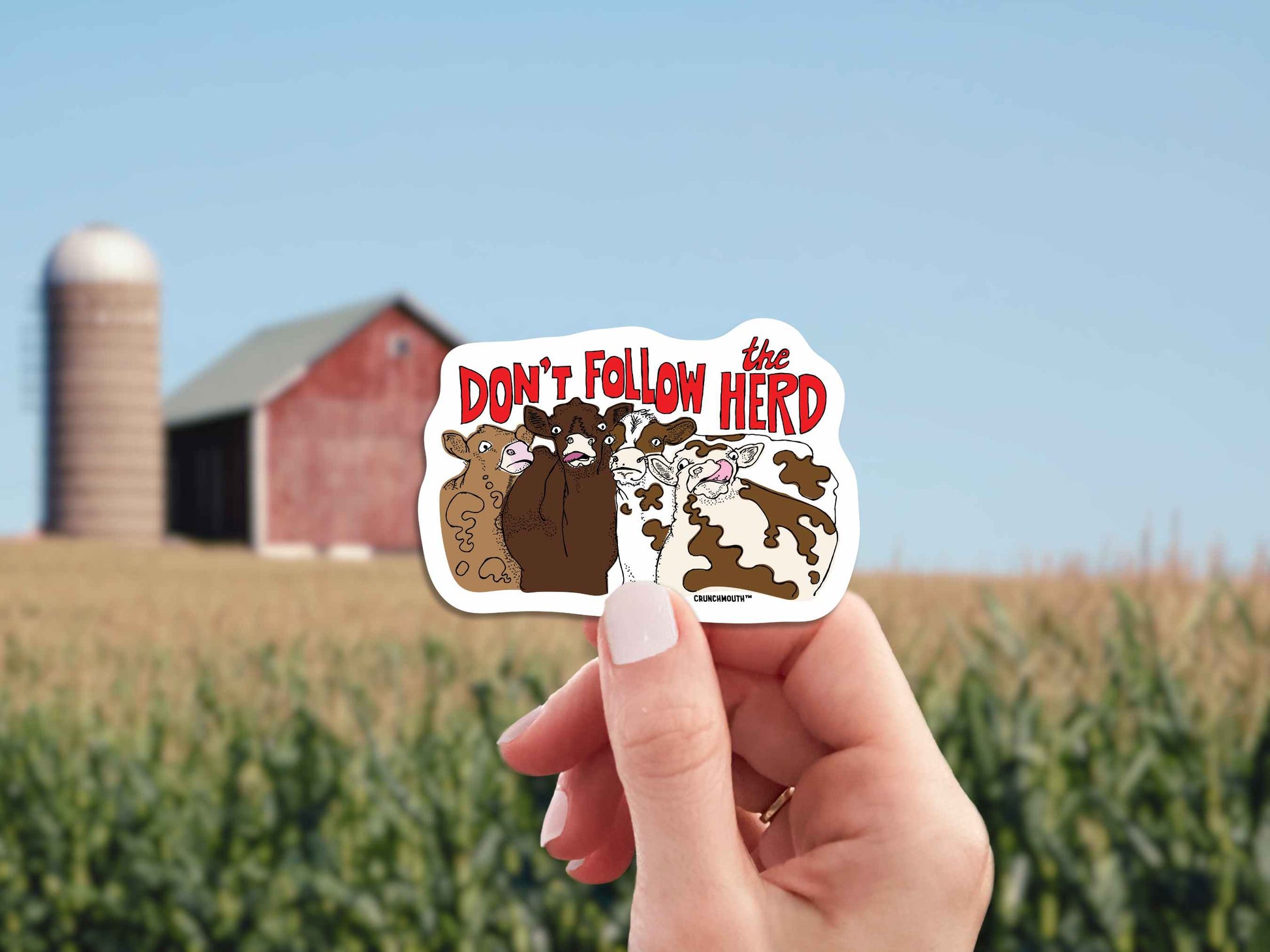 don't follow the herd sticker, hand display, farm red barn background