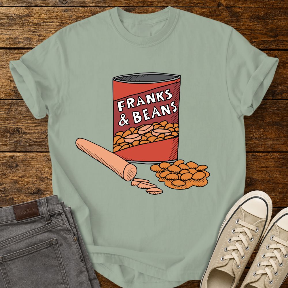 bay green graphic T-shirt mockup featuring a humorous illustration of a can labeled “Franks & Beans” with sliced hot dogs and beans, styled with gray jeans and beige sneakers on a rustic wood background.
