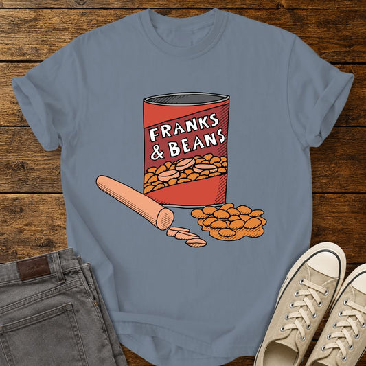 Blue jean graphic T-shirt mockup featuring a humorous illustration of a can labeled “Franks & Beans” with sliced hot dogs and beans, styled with gray jeans and beige sneakers on a rustic wood background.