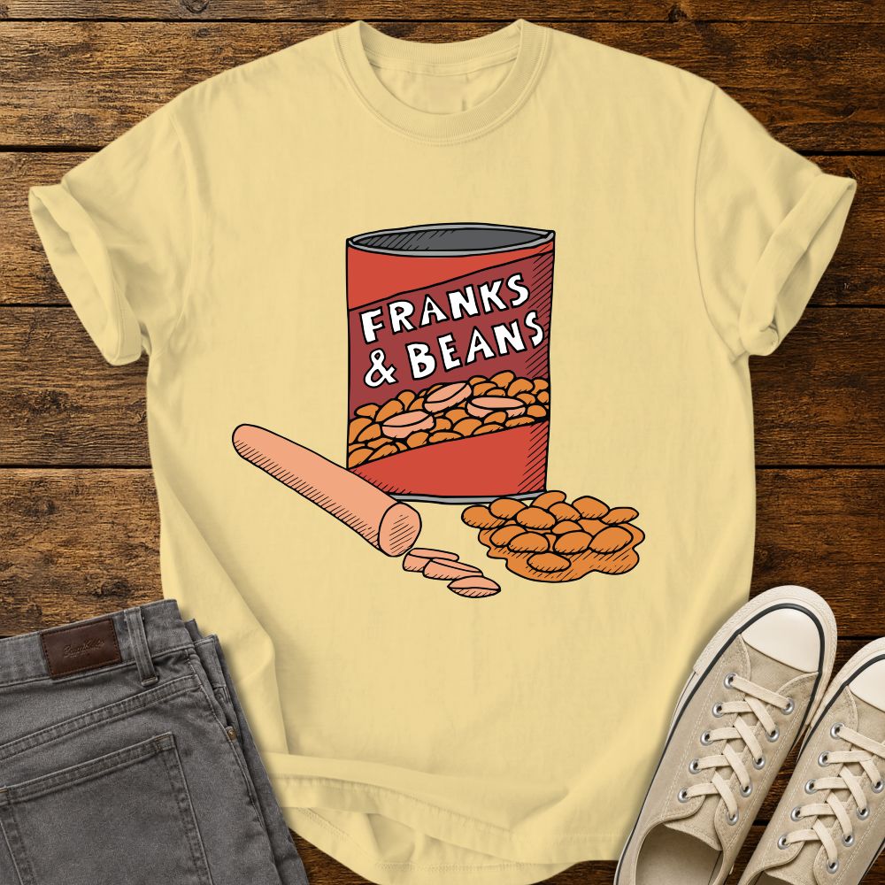 butter yellow graphic T-shirt mockup featuring a humorous illustration of a can labeled “Franks & Beans” with sliced hot dogs and beans, styled with gray jeans and beige sneakers on a rustic wood background.
