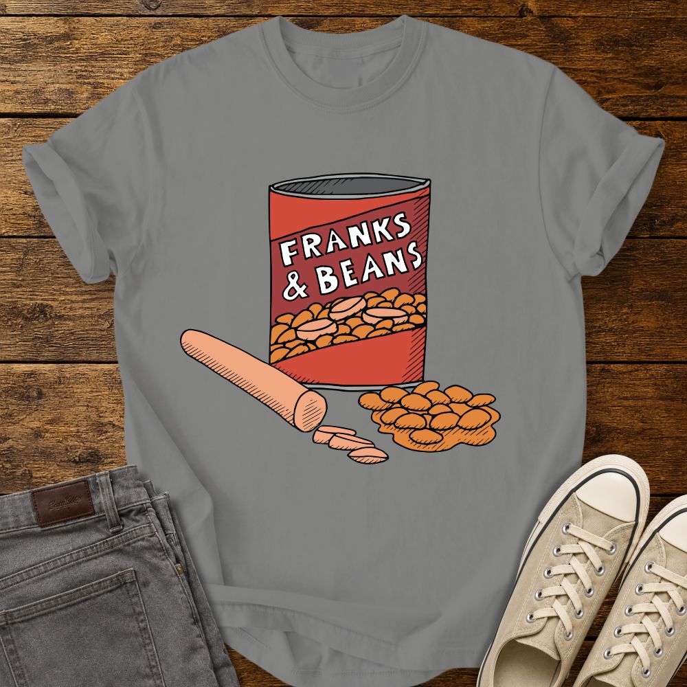 granite graphic T-shirt mockup featuring a humorous illustration of a can labeled “Franks & Beans” with sliced hot dogs and beans, styled with gray jeans and beige sneakers on a rustic wood background.