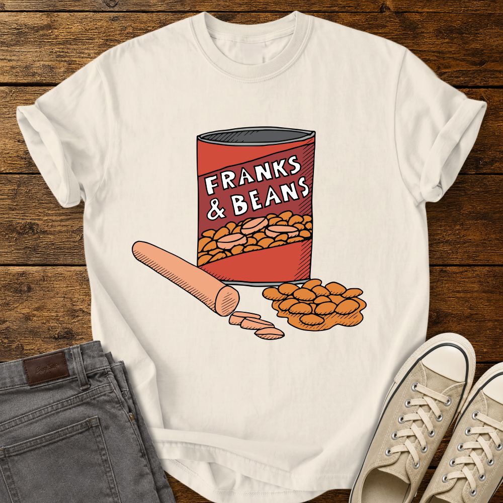 ivory graphic T-shirt mockup featuring a humorous illustration of a can labeled “Franks & Beans” with sliced hot dogs and beans, styled with gray jeans and beige sneakers on a rustic wood background.