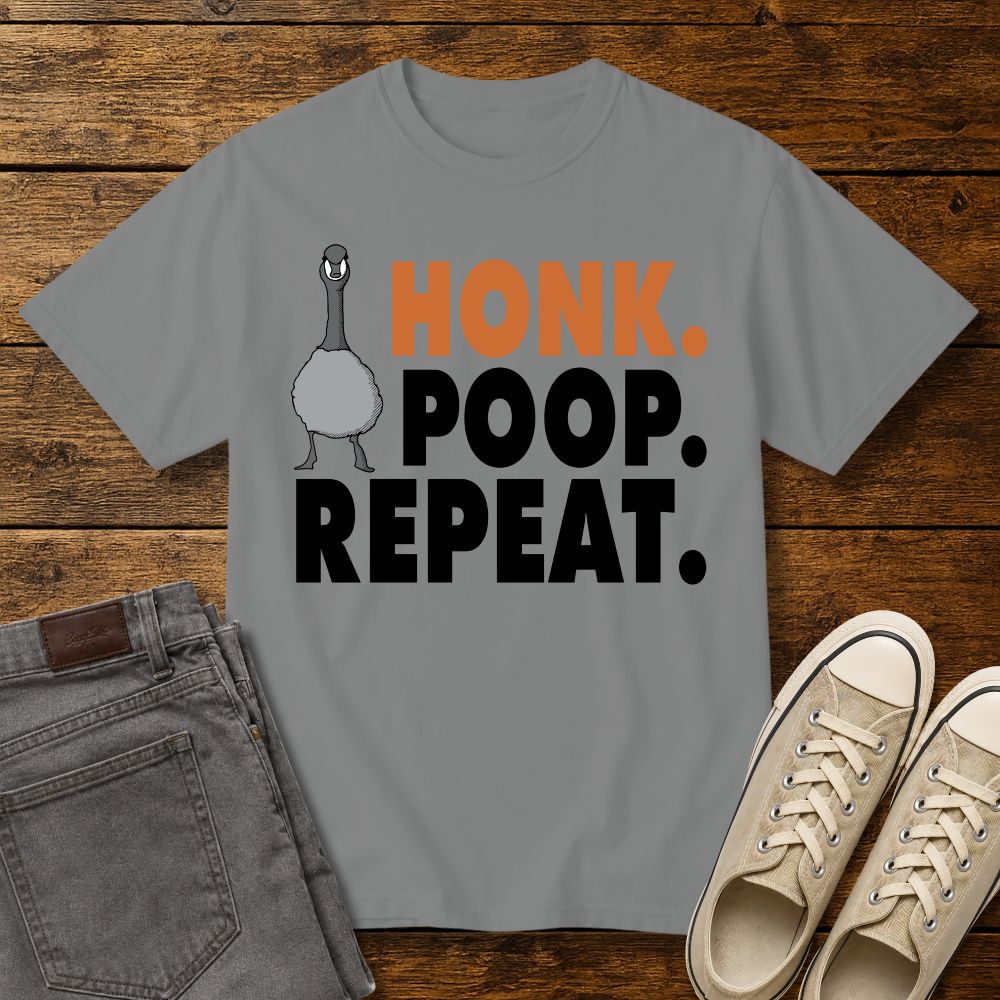grey graphic T-shirt mockup featuring a goose illustration and the phrase “Honk. Poop. Repeat.” in bold orange and black lettering, styled with gray jeans and beige sneakers on a rustic wood background.