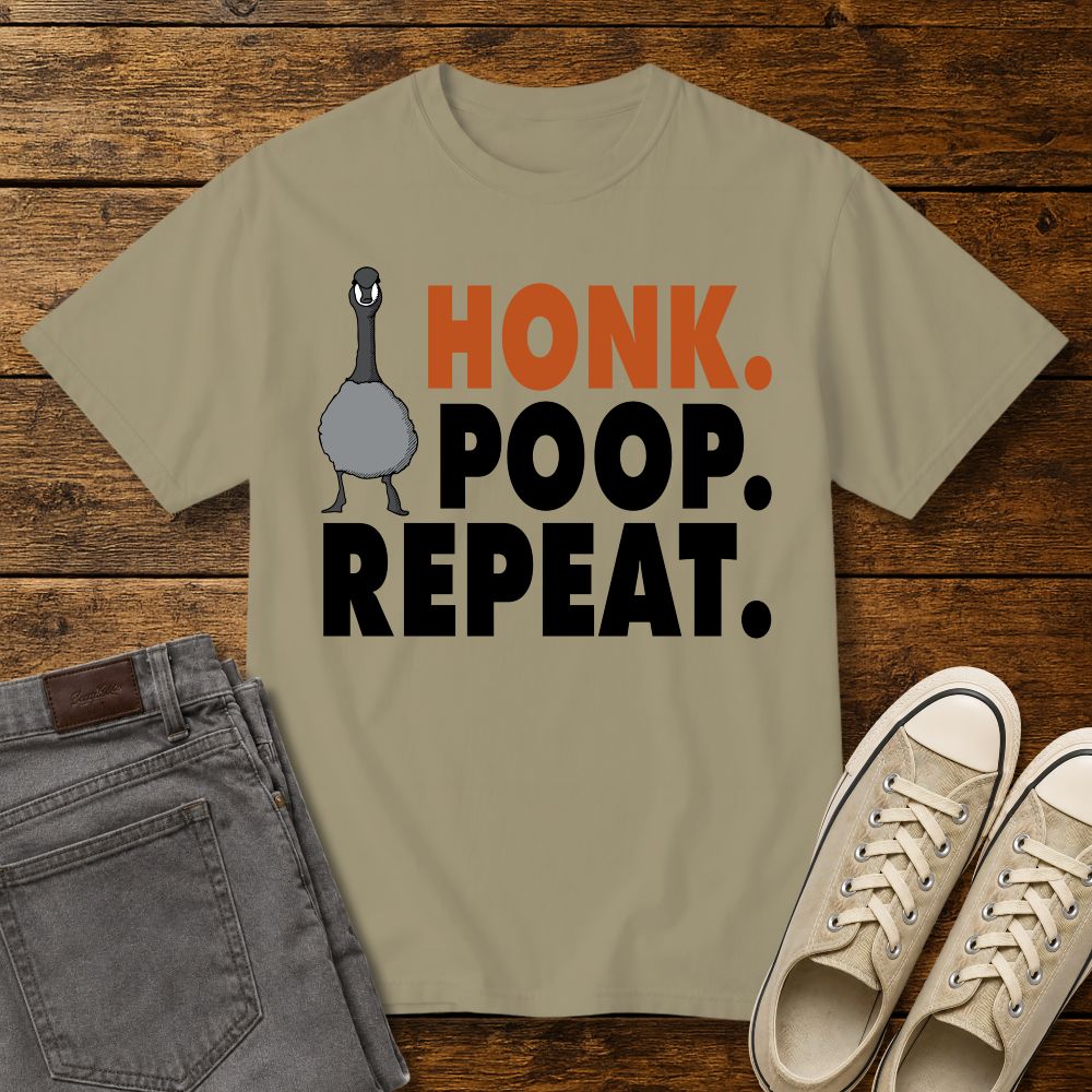 Khaki graphic T-shirt mockup featuring a goose illustration and the phrase “Honk. Poop. Repeat.” in bold orange and black lettering, styled with gray jeans and beige sneakers on a rustic wood background.