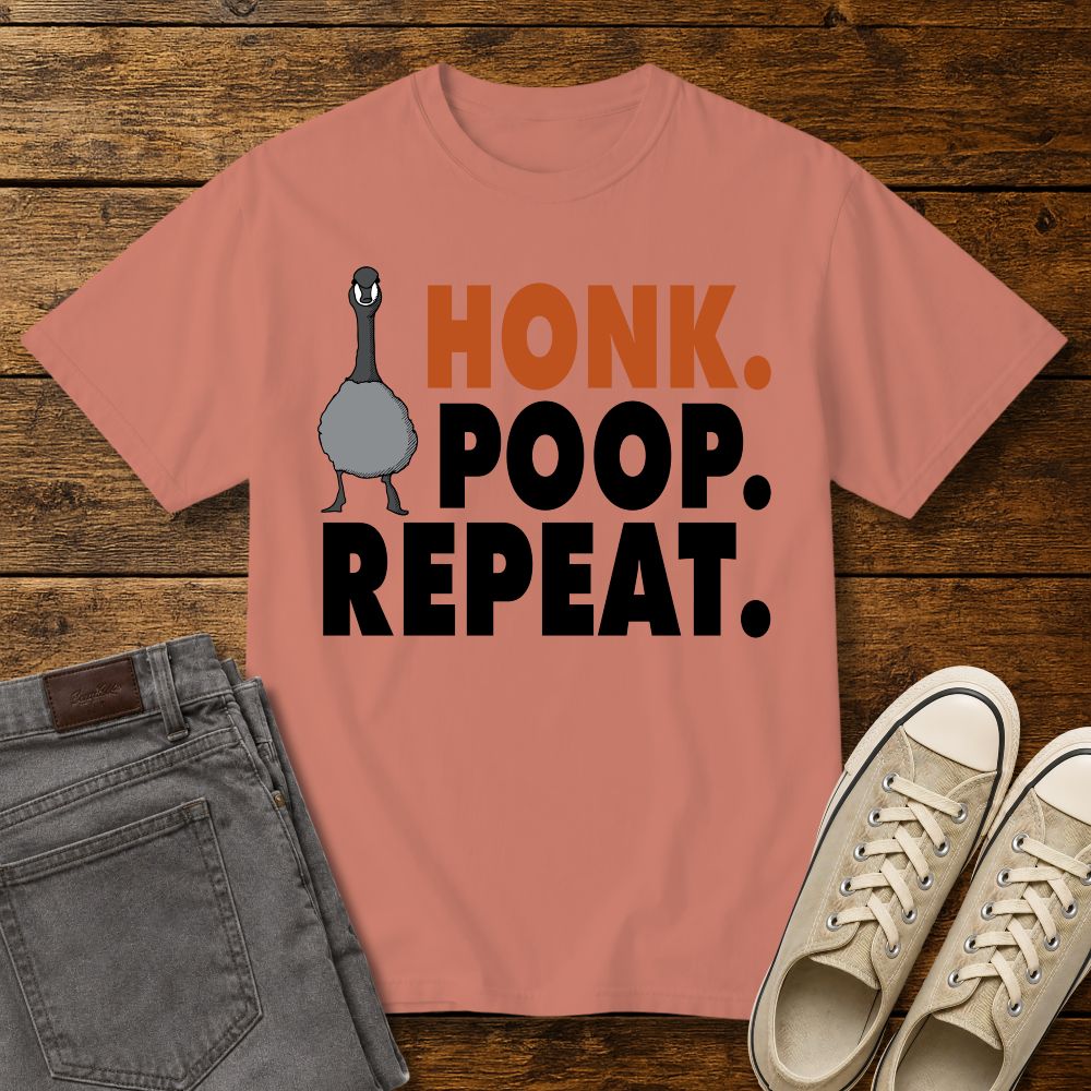 terracotta graphic T-shirt mockup featuring a goose illustration and the phrase “Honk. Poop. Repeat.” in bold orange and black lettering, styled with gray jeans and beige sneakers on a rustic wood background.