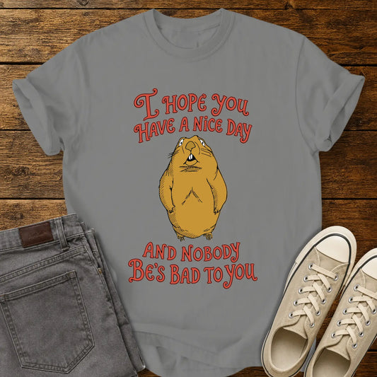Granite gray graphic T-shirt mockup featuring a groundhog illustration between the phrases “I Hope You Have a Nice Day” and “And Nobody Be’s Bad to You” in vintage-style red lettering, styled with gray jeans and beige sneakers on a rustic wood background.