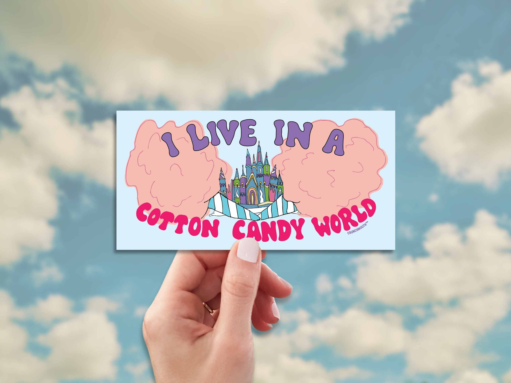 i live in a cotton candy world bumper sticker, hand display, blue sky with clouds background