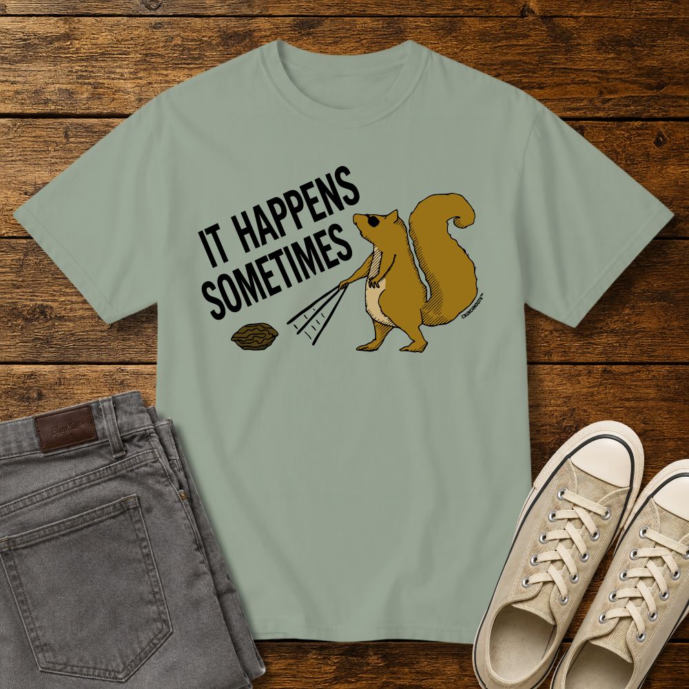 Funny squirrel graphic t-shirt on sage green tee with ‘It Happens Sometimes’ text, shown in flat lay mockup with jeans and sneakers on rustic wood background