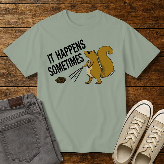 Funny squirrel graphic t-shirt on sage green tee with ‘It Happens Sometimes’ text, shown in flat lay mockup with jeans and sneakers on rustic wood background