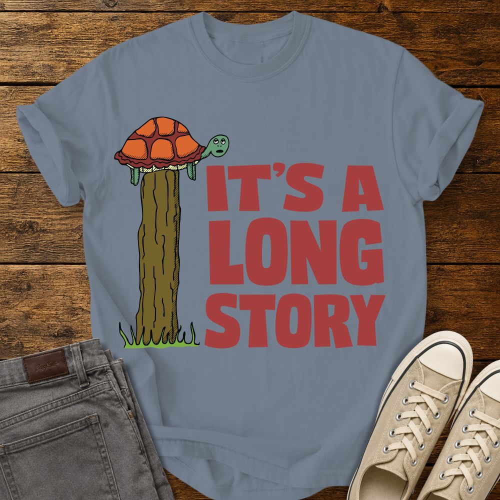 blue jean graphic T-shirt mockup featuring a turtle sitting on top of a tall fence post beside the phrase “It’s a Long Story” in large red lettering, styled with gray jeans and beige sneakers on a rustic wood background.