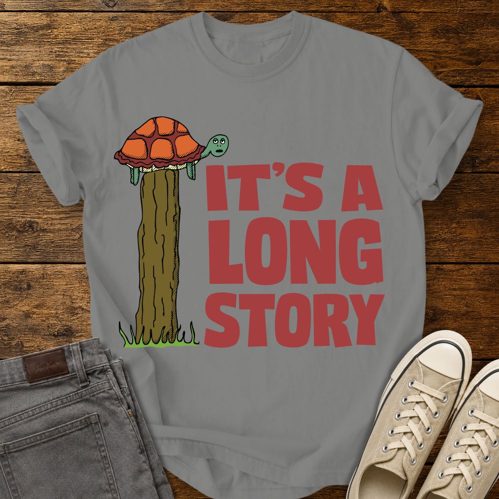 granite grey graphic T-shirt mockup featuring a turtle sitting on top of a tall fence post beside the phrase “It’s a Long Story” in large red lettering, styled with gray jeans and beige sneakers on a rustic wood background.