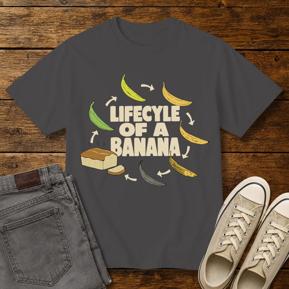 graphite color graphic T-shirt mockup featuring the phrase “Lifecycle of a Banana” surrounded by illustrations of bananas ripening into banana bread, styled with gray jeans and beige sneakers on a rustic wood background.