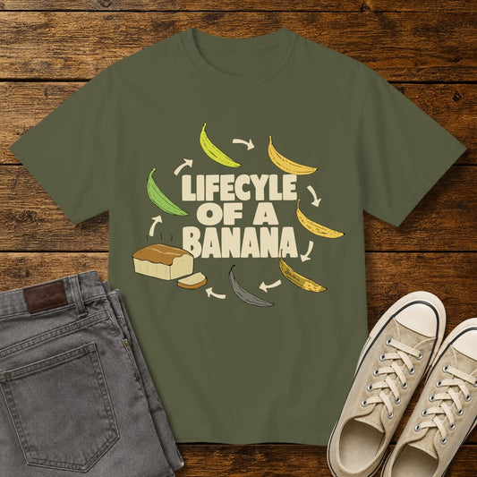 Hemp green graphic T-shirt mockup featuring the phrase “Lifecycle of a Banana” surrounded by illustrations of bananas ripening into banana bread, styled with gray jeans and beige sneakers on a rustic wood background.