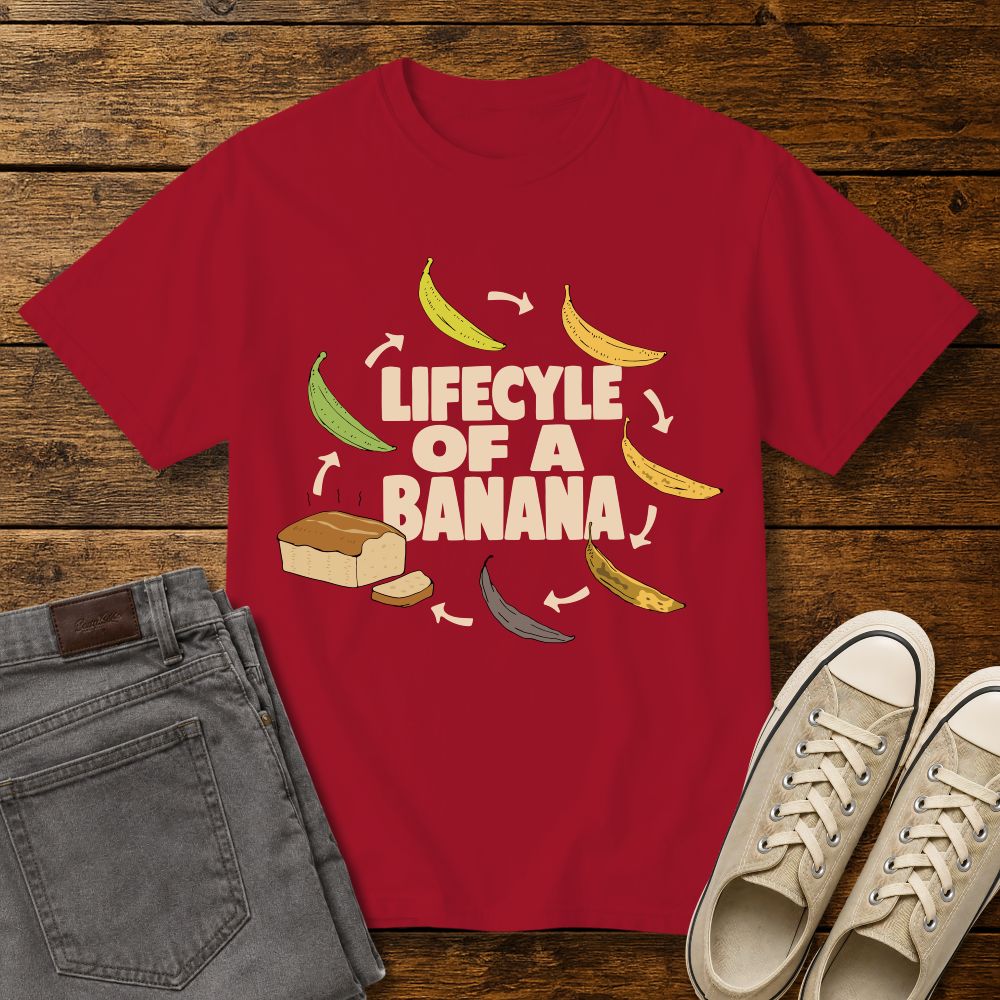 red graphic T-shirt mockup featuring the phrase “Lifecycle of a Banana” surrounded by illustrations of bananas ripening into banana bread, styled with gray jeans and beige sneakers on a rustic wood background.