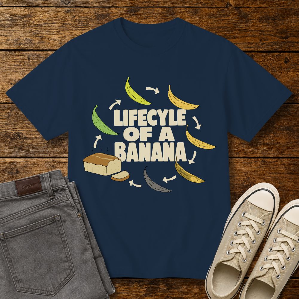 true navy blue graphic T-shirt mockup featuring the phrase “Lifecycle of a Banana” surrounded by illustrations of bananas ripening into banana bread, styled with gray jeans and beige sneakers on a rustic wood background.