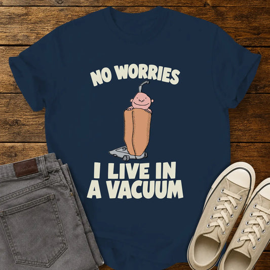 True navy graphic T-shirt mockup featuring a cartoon person riding inside a vacuum cleaner bag with the phrase “No Worries, I Live in a Vacuum” in bold white lettering, styled with gray jeans and beige sneakers on a rustic wood background.