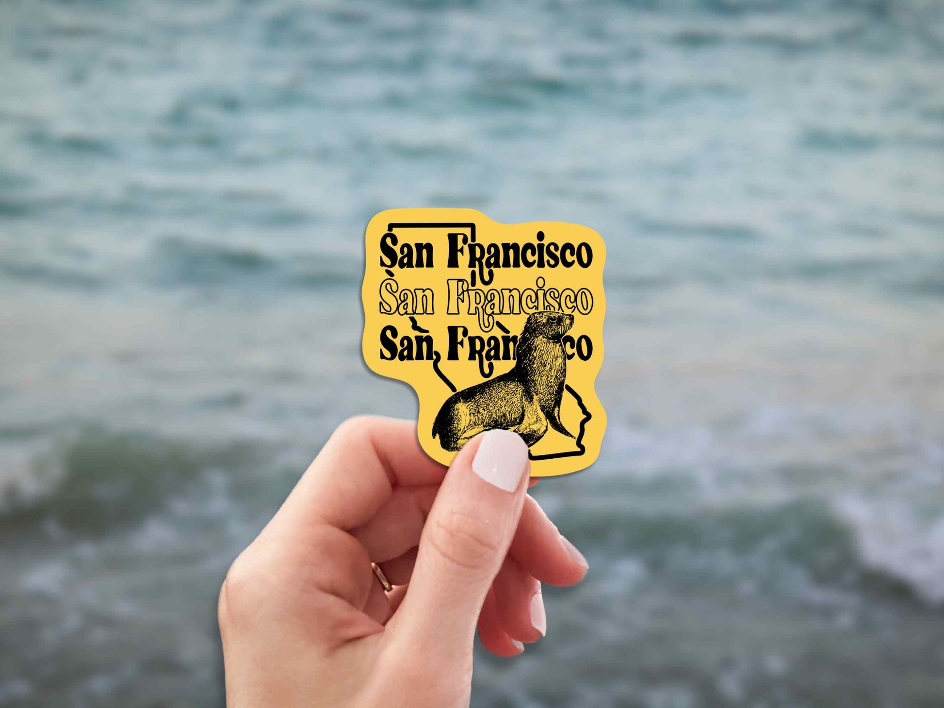 san francisco travel luggage sticker, hand display, blurred ocean water background