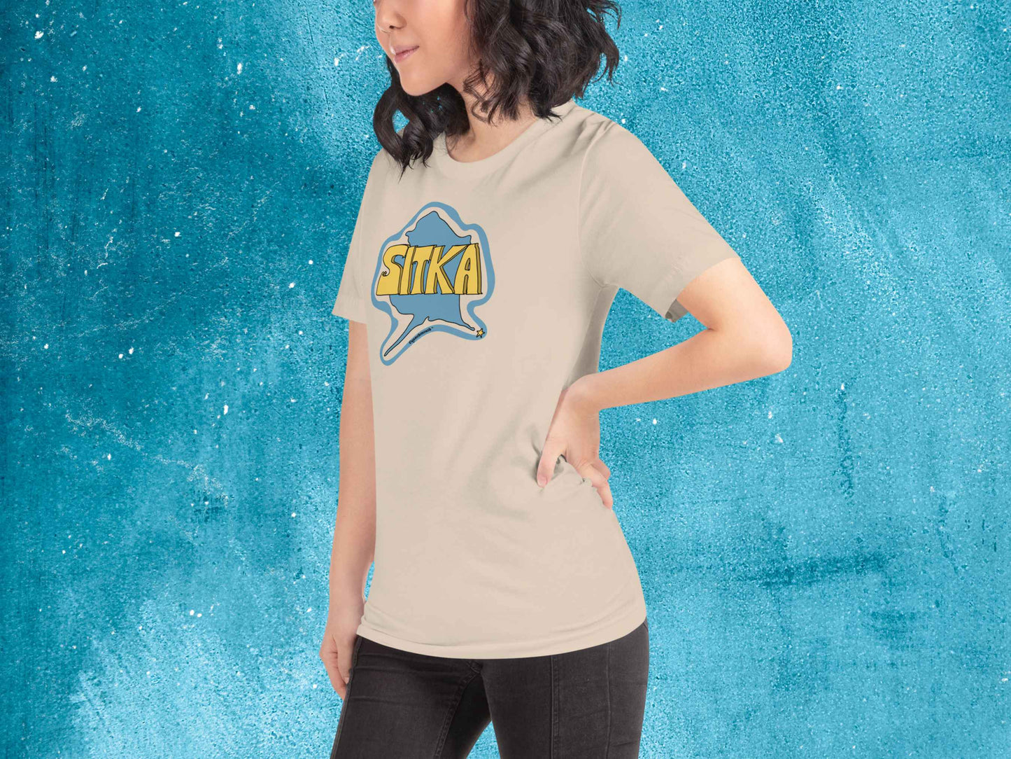 sitka shirt, souvenir t shirts, female model, front left, blue textured background