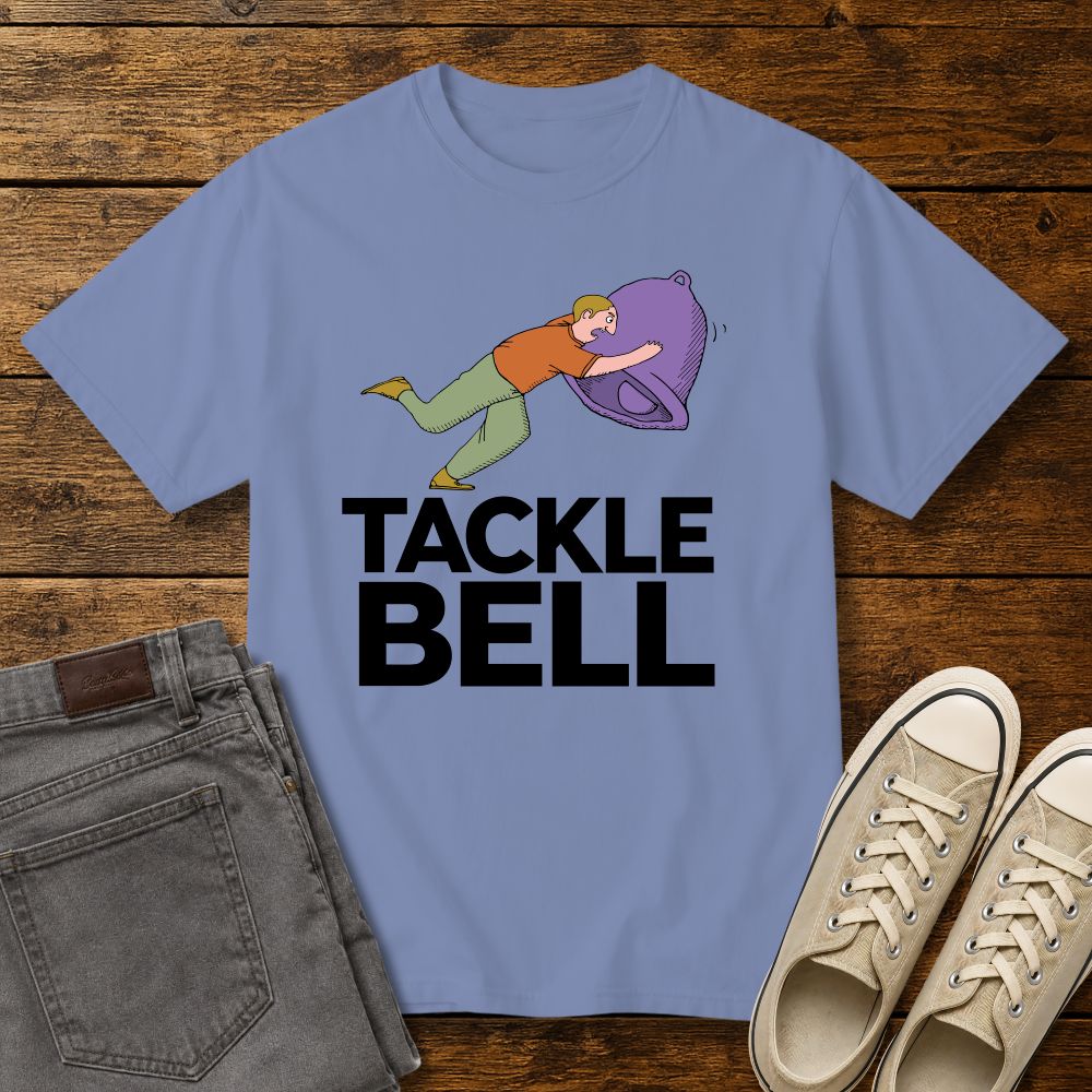 washed denim blue graphic T-shirt mockup featuring a cartoon-style man tackling a large bell with the phrase “Tackle Bell” in bold black lettering, styled with gray jeans and beige sneakers on a rustic wood background.